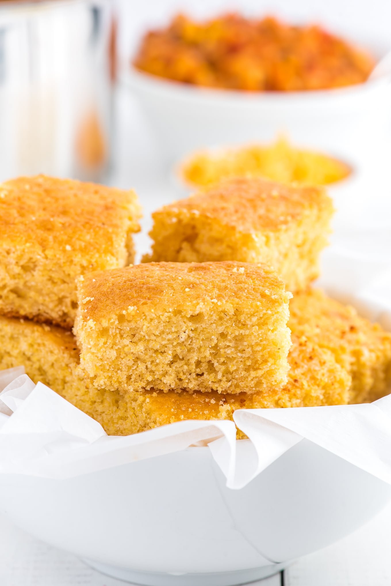 A white bowl with squares of honey sweetened cornbread on the table. 