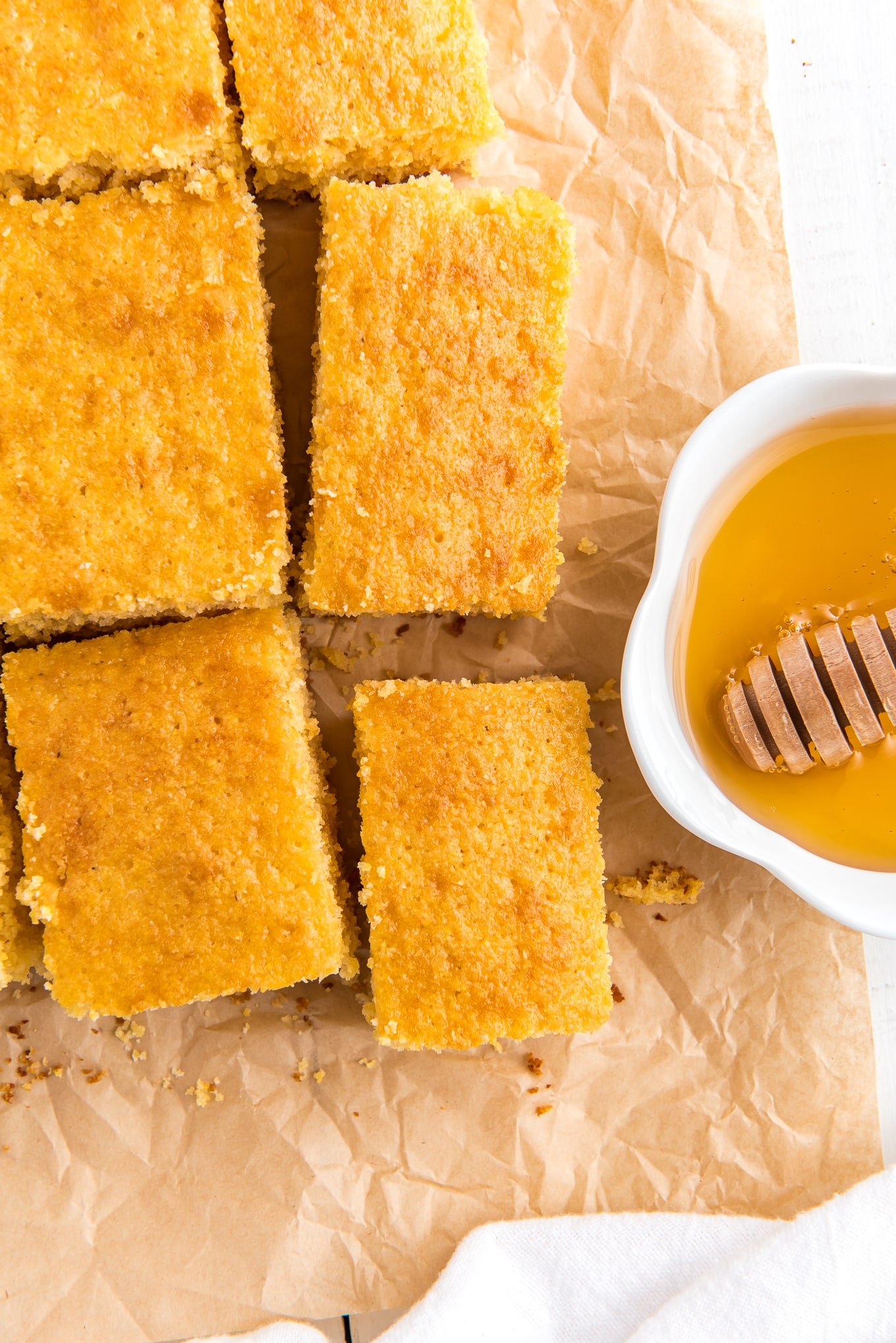 Squares of cornbread oil-free on the table with a bowl of honey next to it.