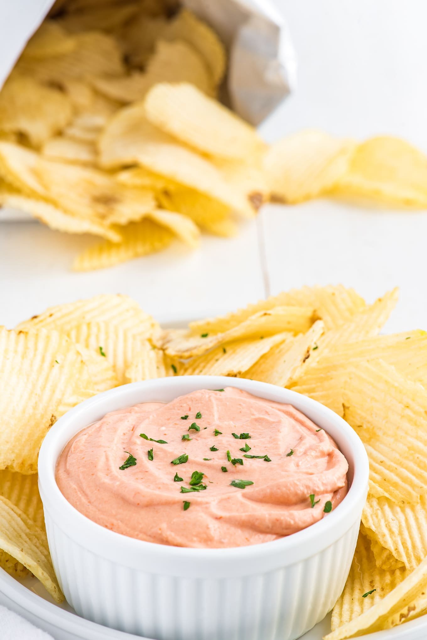 A shot of small bowl of potato chip dip with chips in the background.