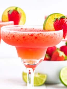 Strawberry margarita in a glass with strawberry and lime garnish.