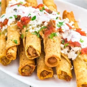 taquitos cooked in the air fryer served on a plate topped with queso, pico de gallo and salsa.