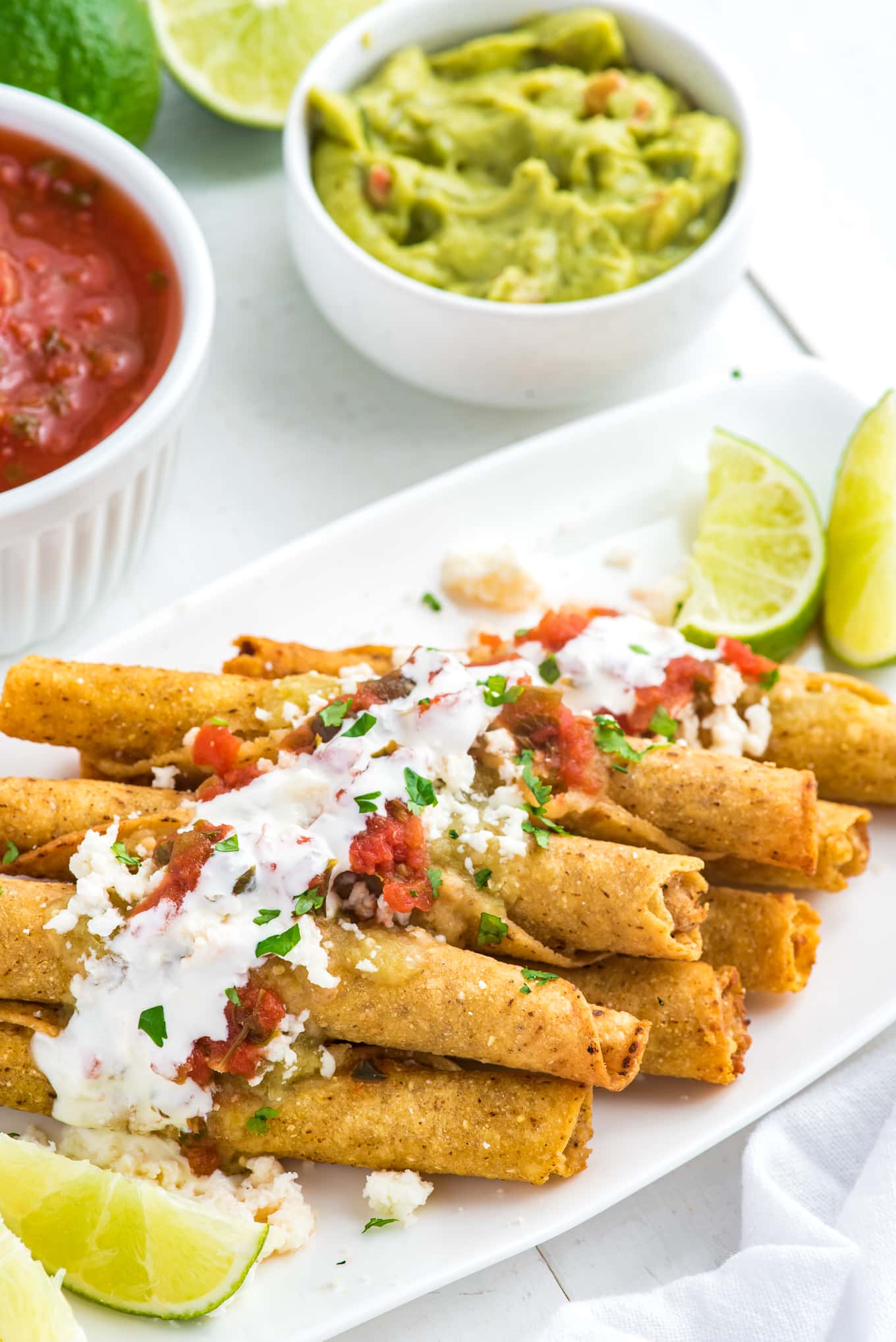 taquitos made in the air fryer on a plate with guucamole and salsa on the side. 