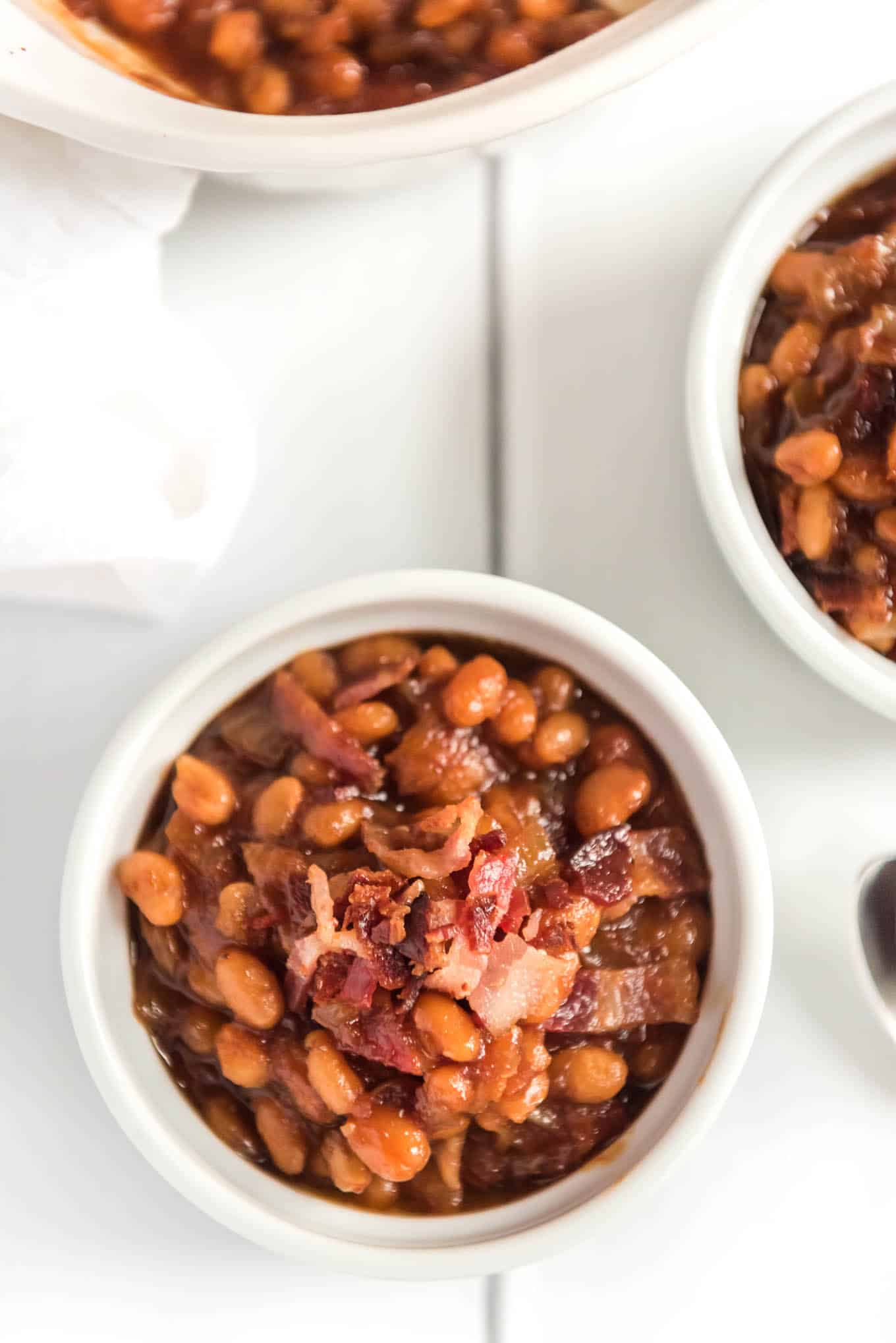 Small ramekin of baked beans with bacon on the counter.