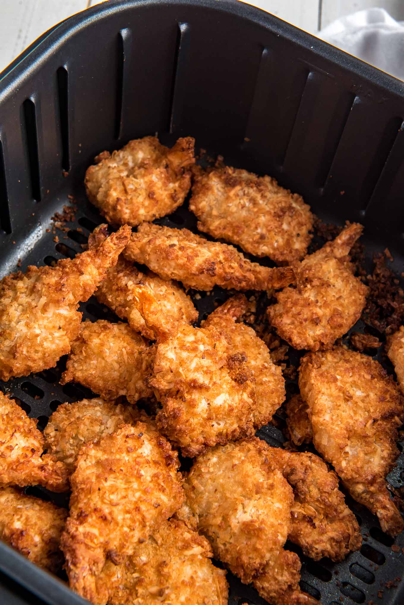 Air fryer basket with cooked breaded shrimp at the bottom of it. 