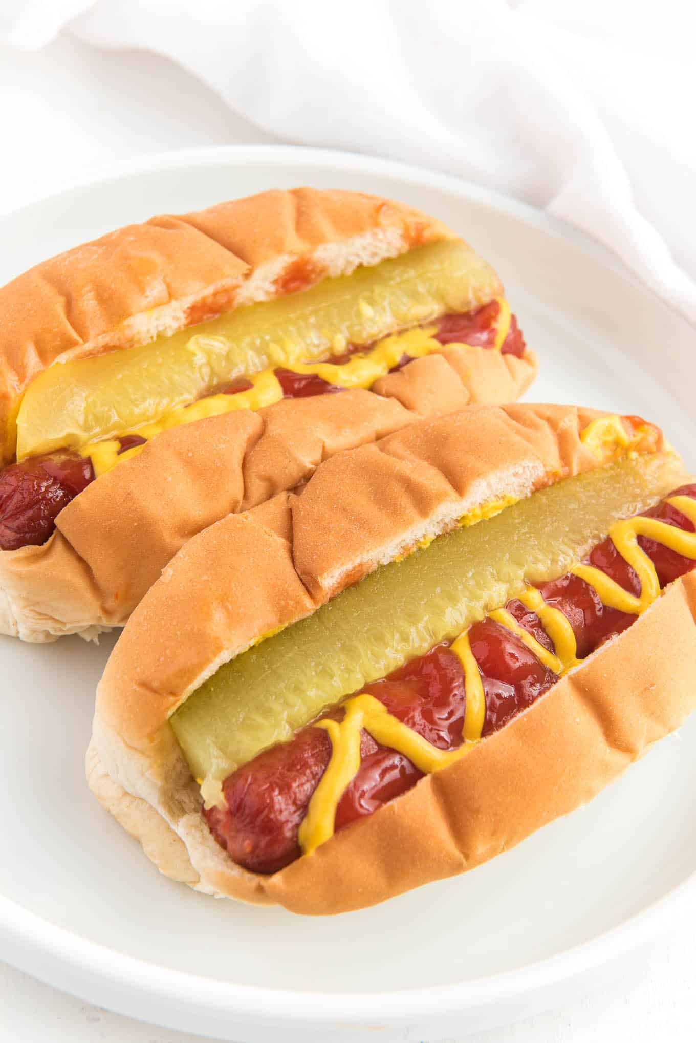 Hot dogs in a bun with a pickle, mustard, and ketchup on top. 