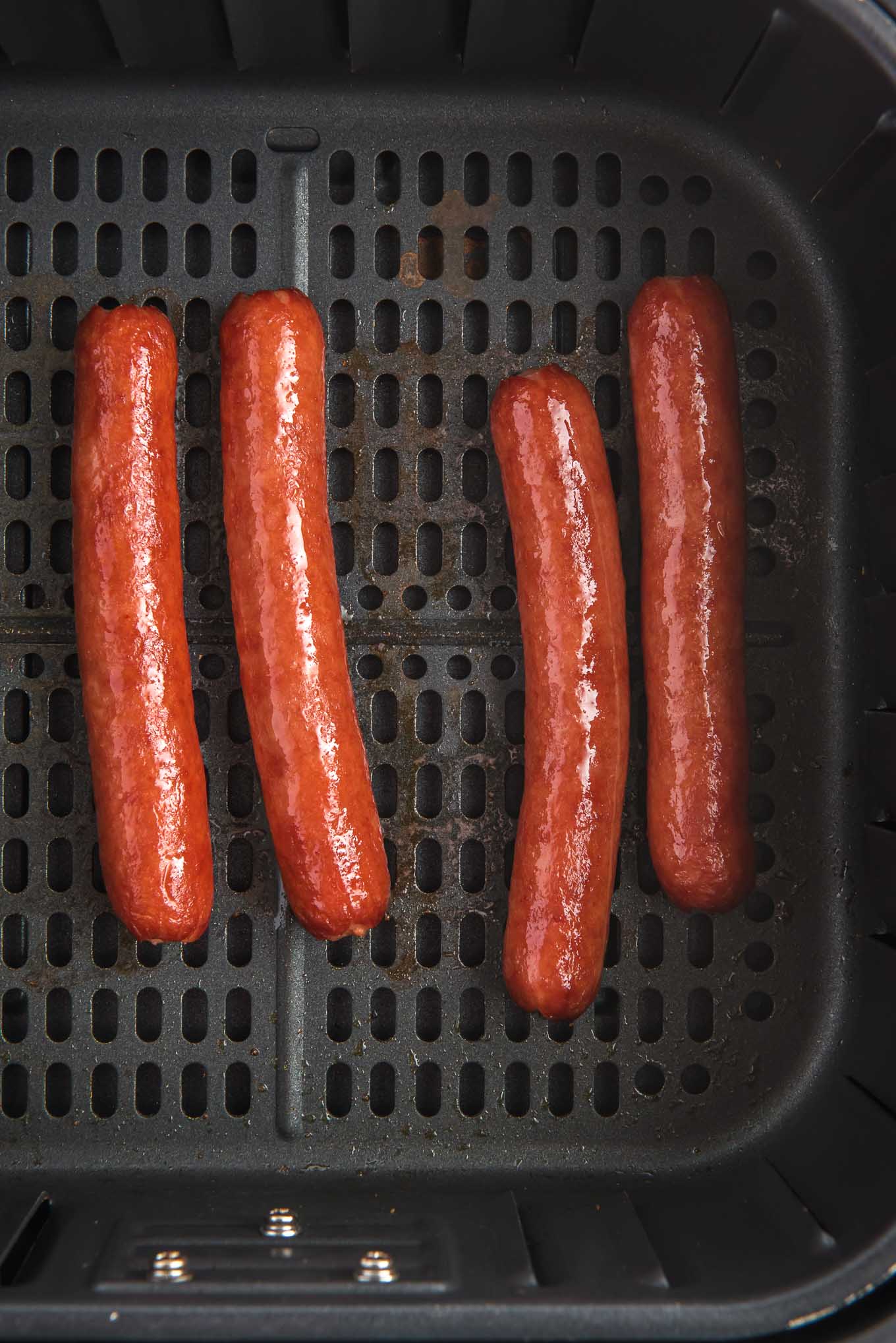 Hot dogs cooked at the bottom of an air fryer basket. 