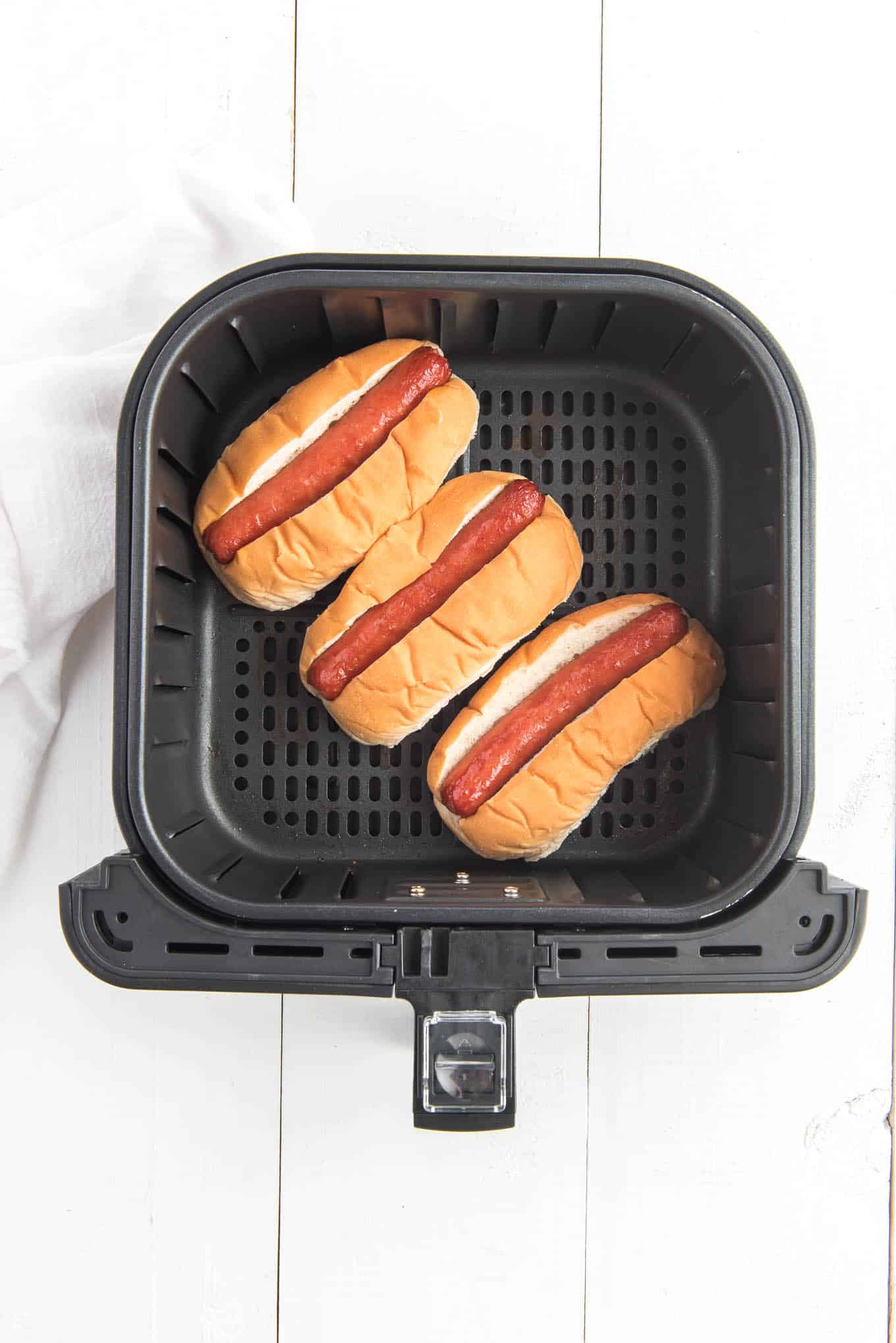 Hot dogs in the bottom of an air fryer basket in buns. 