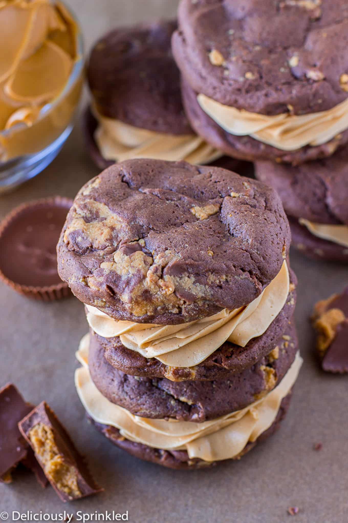 Chocolate peanut butter whoopie pies stacked on the counter with crumbled peanut butter cups.