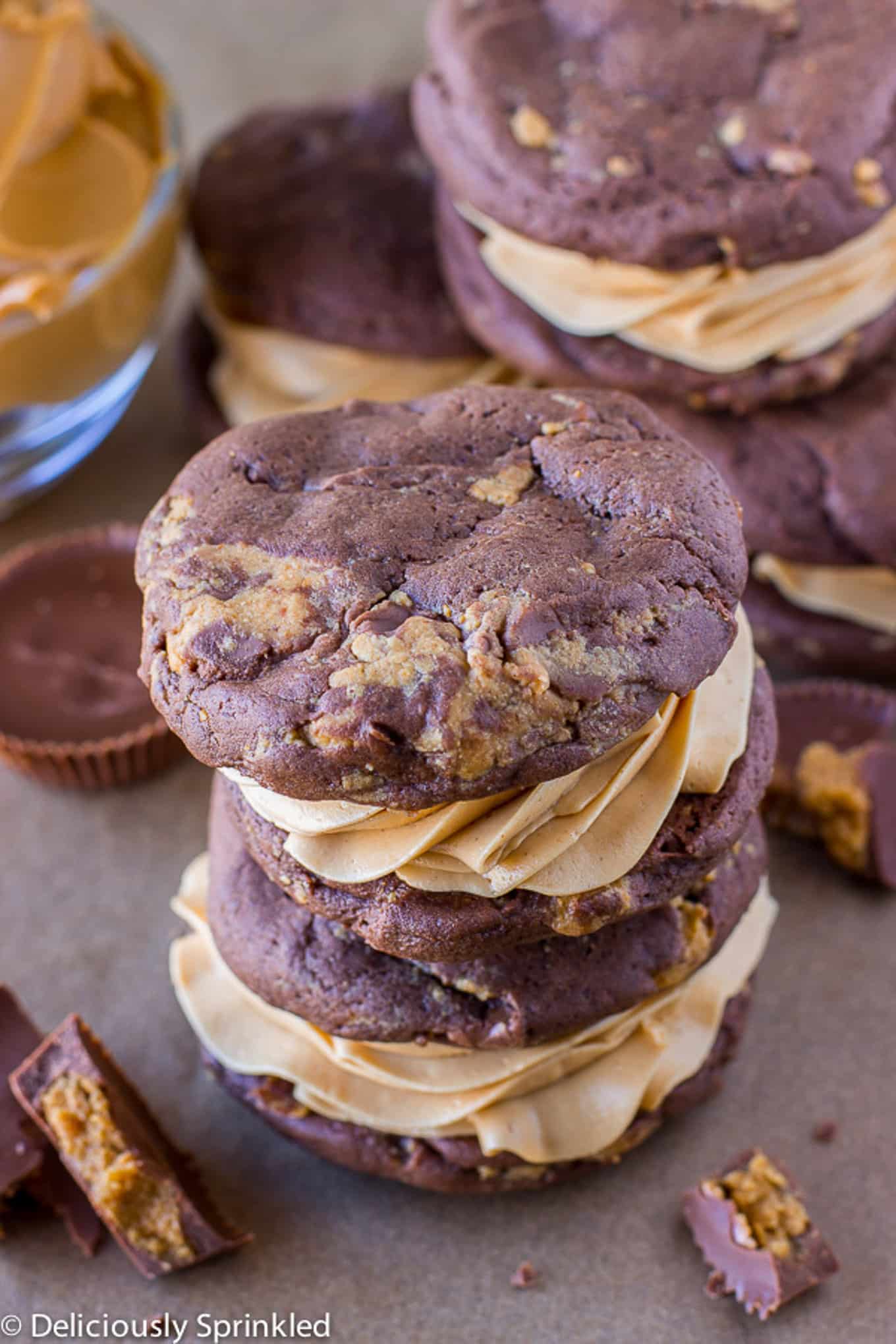 Chocolate peanut butter whoopie pies stacked on the counter with crumbled peanut butter cups.