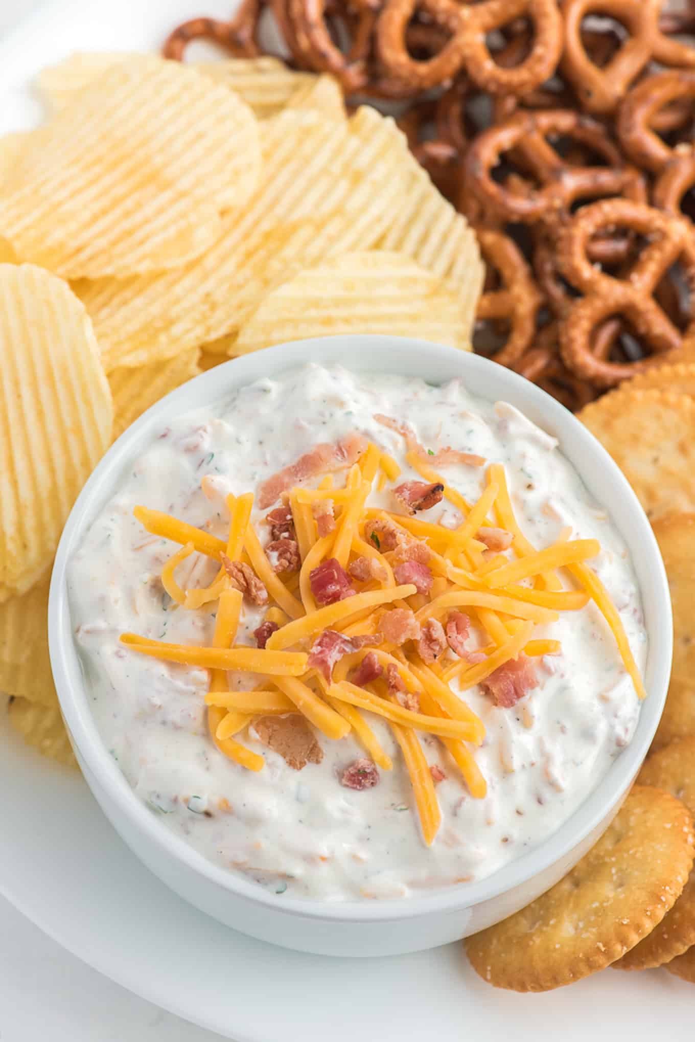 Above shot of crack dip surrounded by chips and pretzels. 