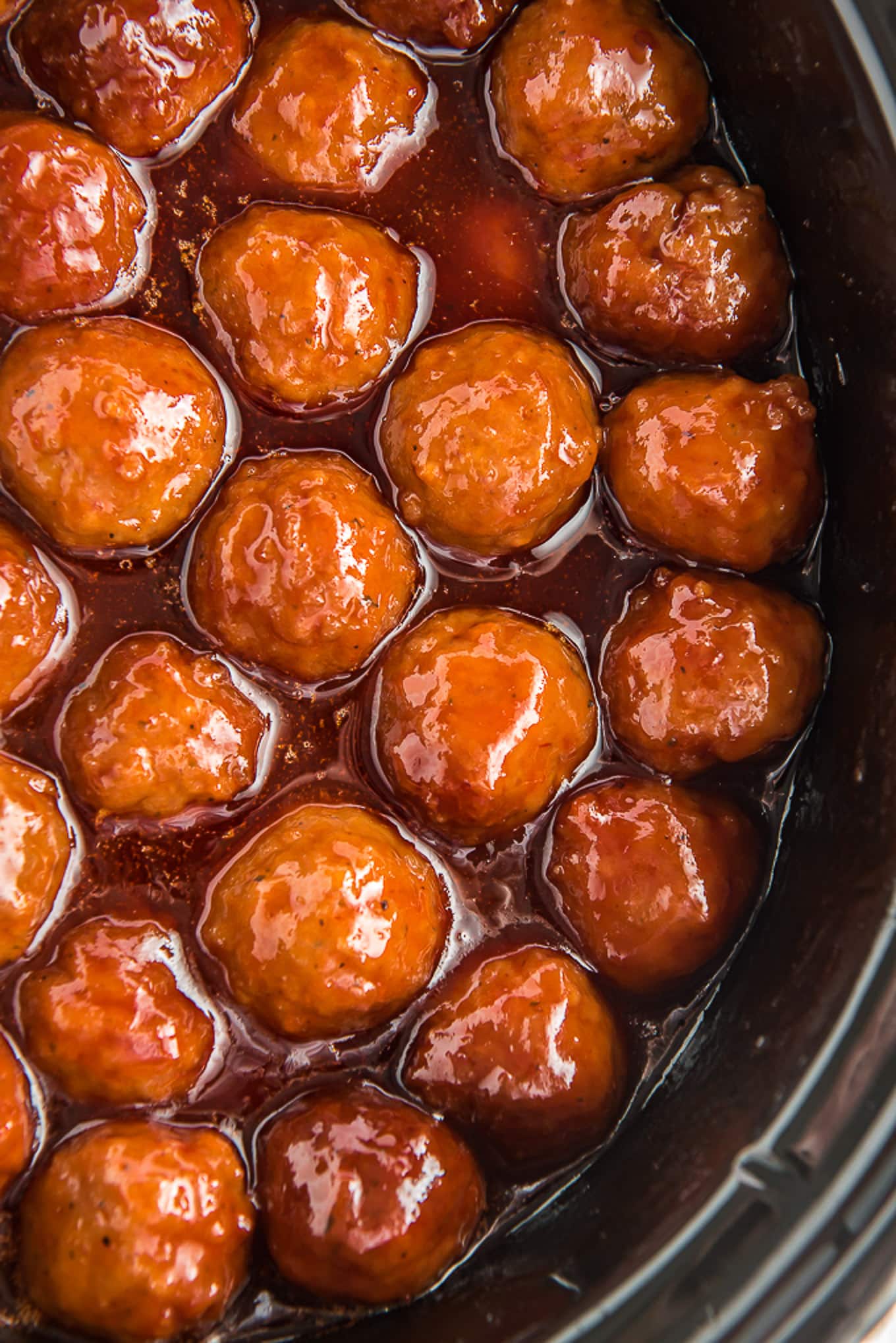 A closeup of frozen meatballs in the crockpot covered in sauce.