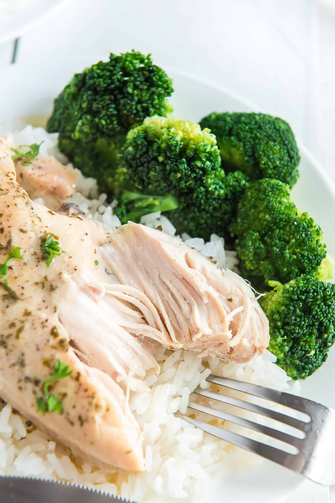 crockpot chicken on a plate with rice and broccoli on the side. Fork cutting chicken breast. 