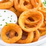 Onion rings made in the air fryer on a plate with a side of ranch dressing.