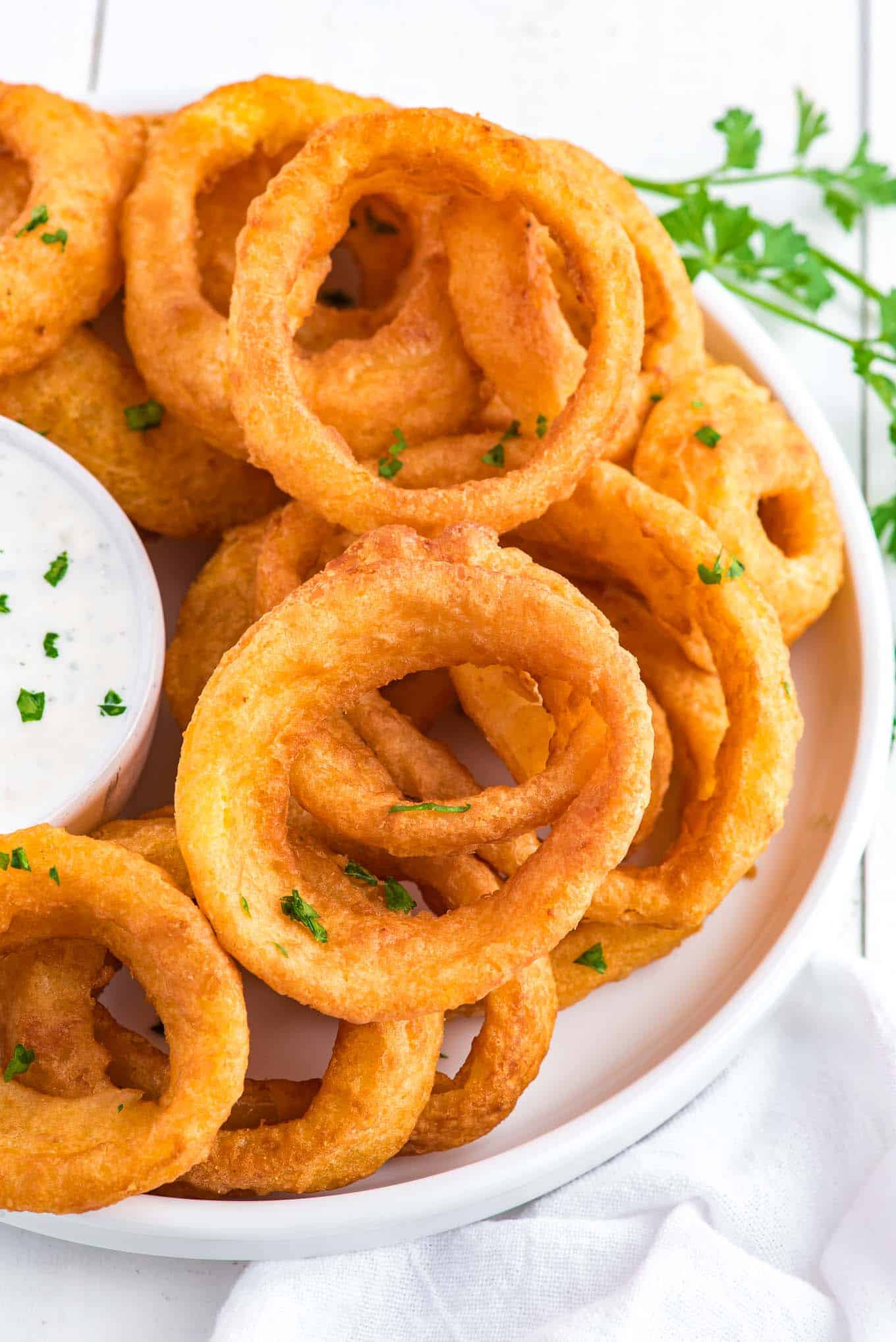A pile of cooked air fryer onion rings on the table with a bowl of ranch.