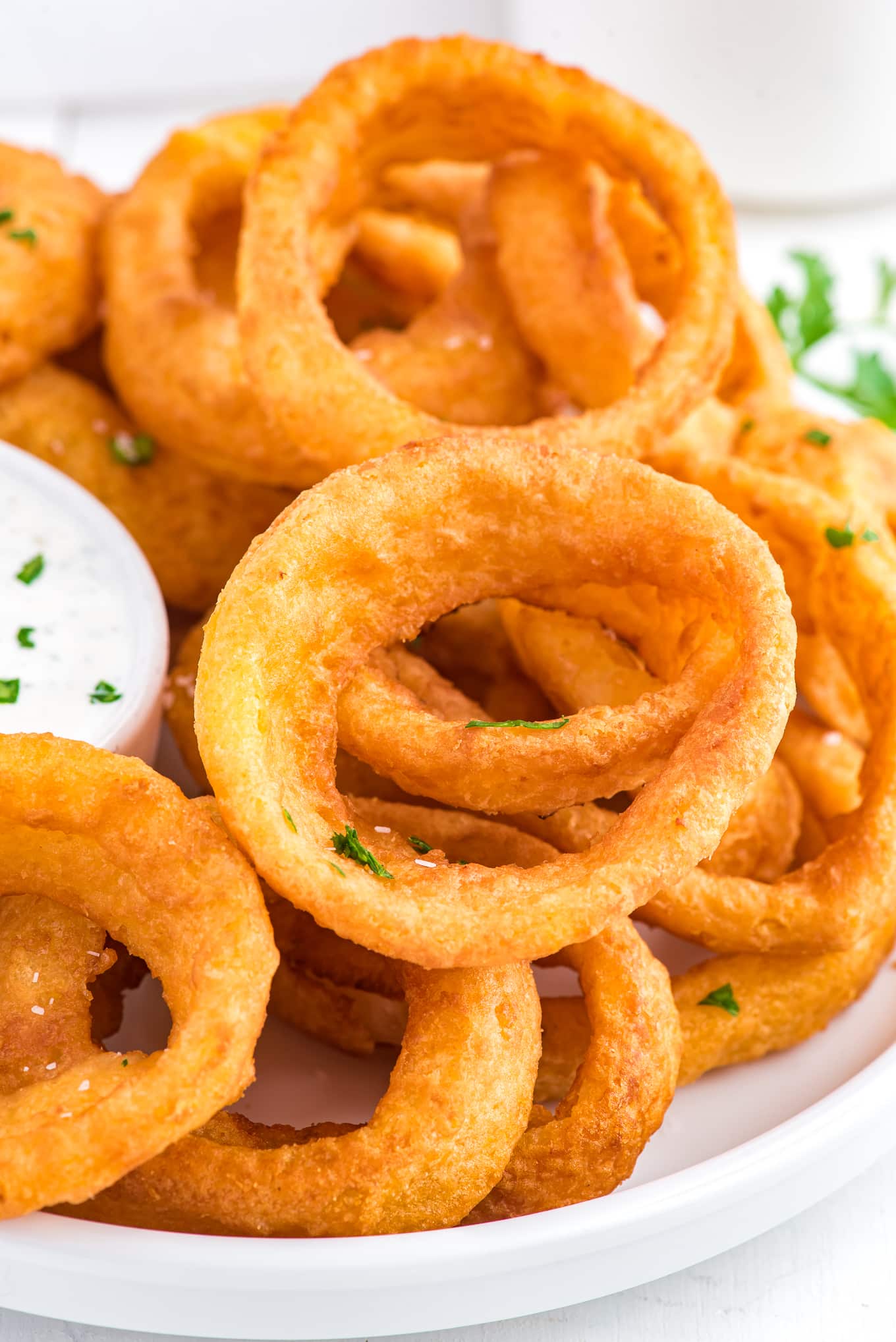 Frozen onion rings in the air fryer served up on a platter with dip and garnished with parsley.