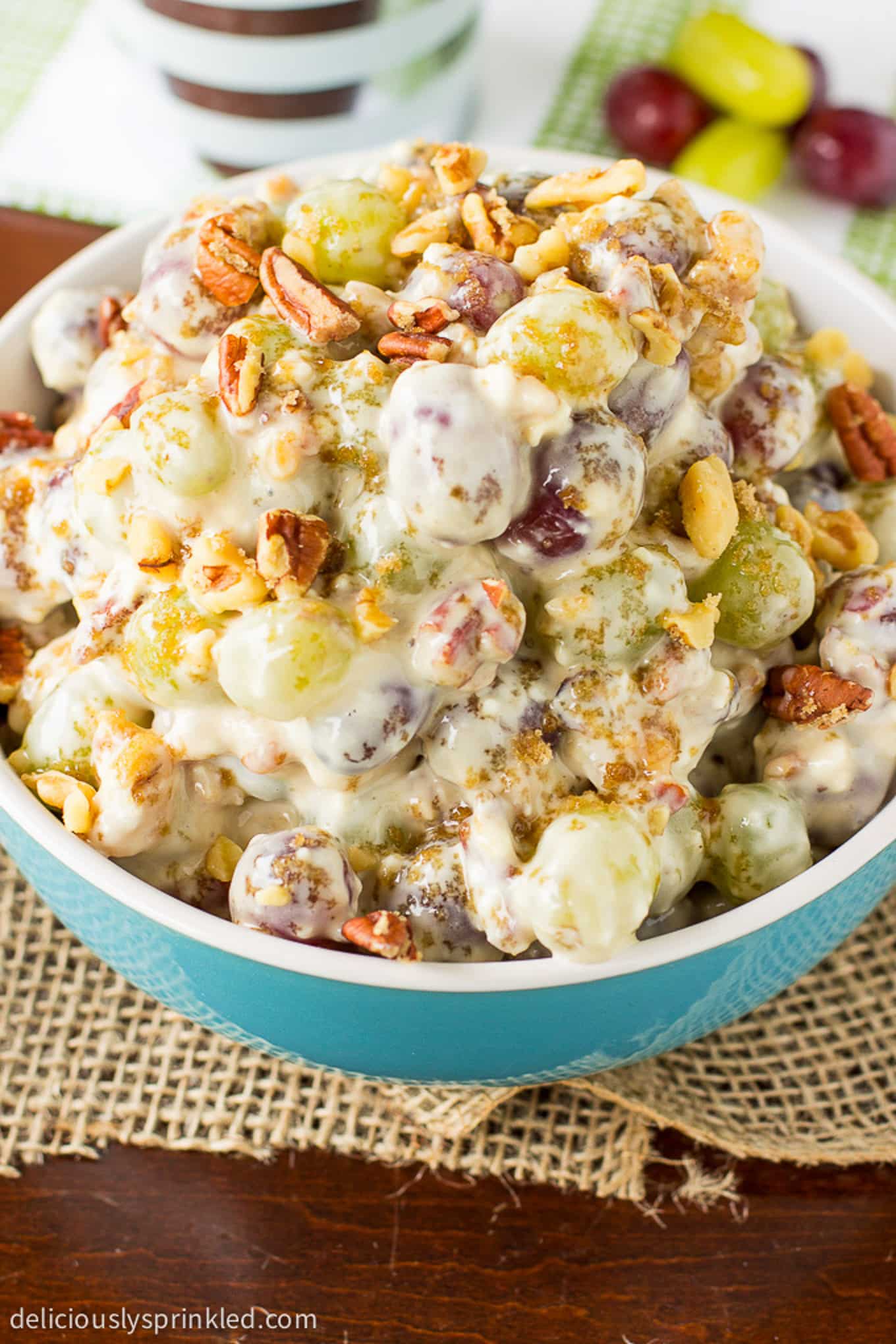 A bowl of grape salad on the table with brown sugar and pecan topping.