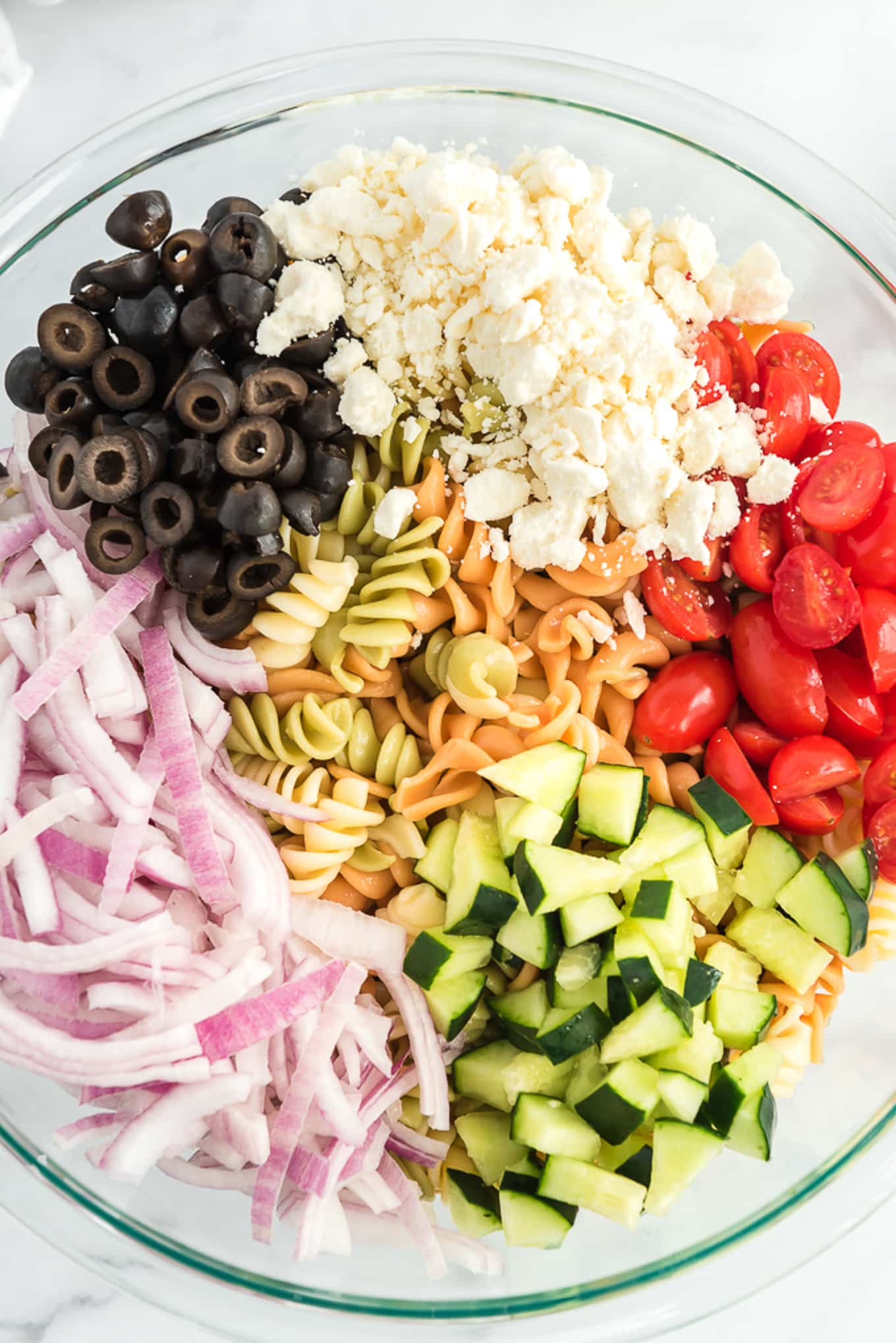 A bowl of pasta topped with chopped vegetables to make a Greek salad with pasta.
