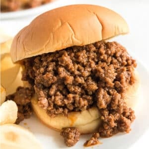 A sloppy joe on a bun with potato chips on a plate.