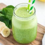 A spinach banana smoothie on a cutting board with fresh bananas and spinach.