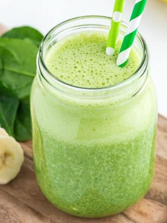A spinach banana smoothie on a cutting board with fresh bananas and spinach.