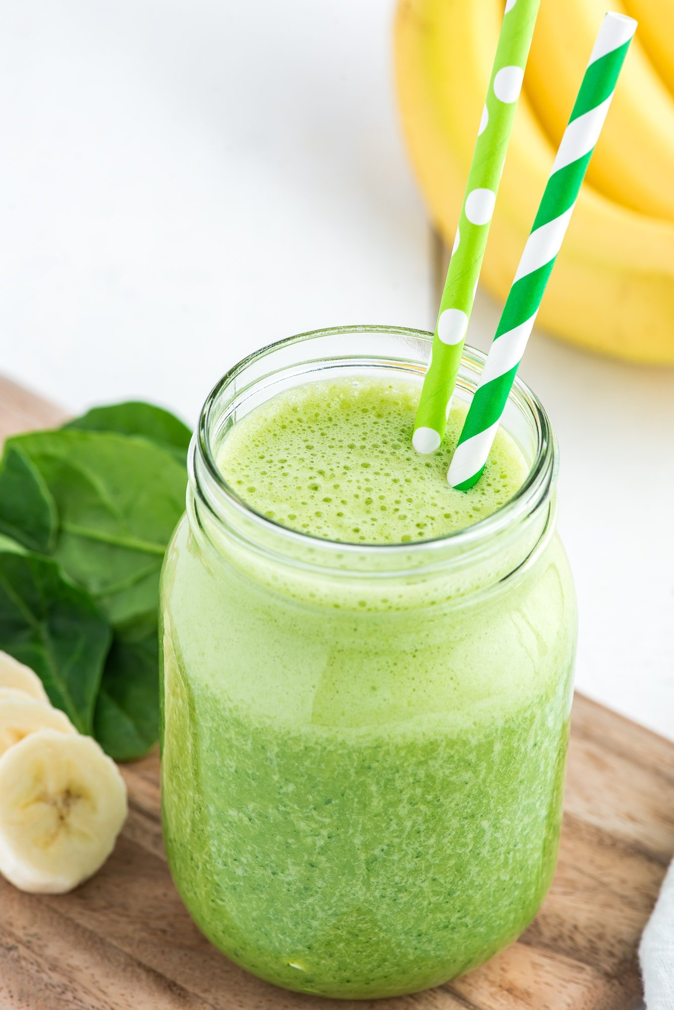 A green smoothie with spinach leaves and green striped and polka dot straws.
