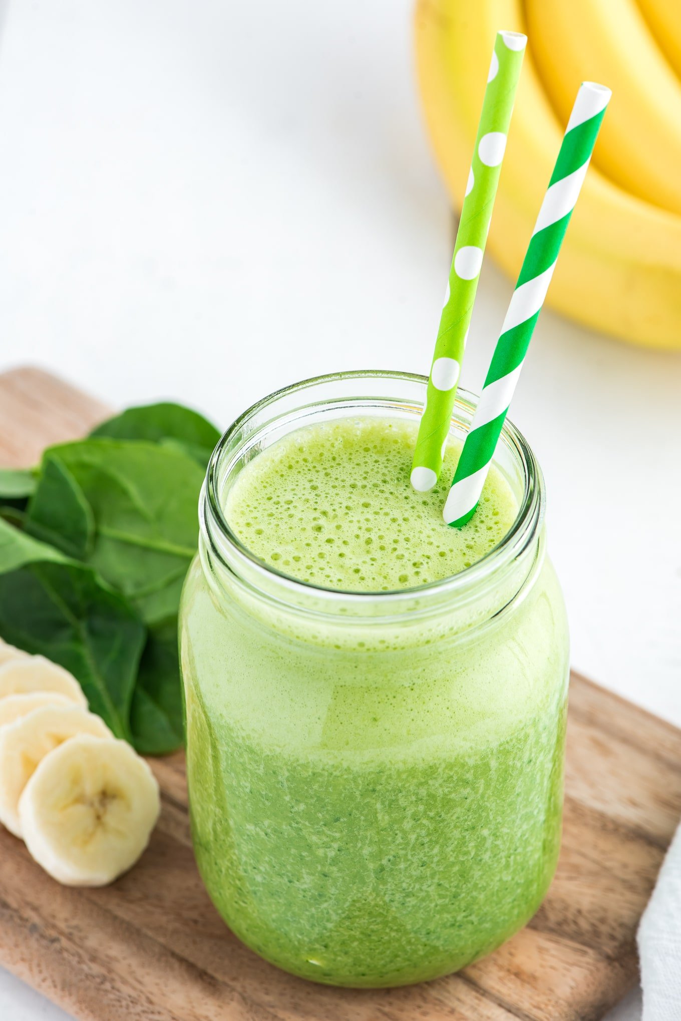 Spinach smoothie in a glass with two straws.