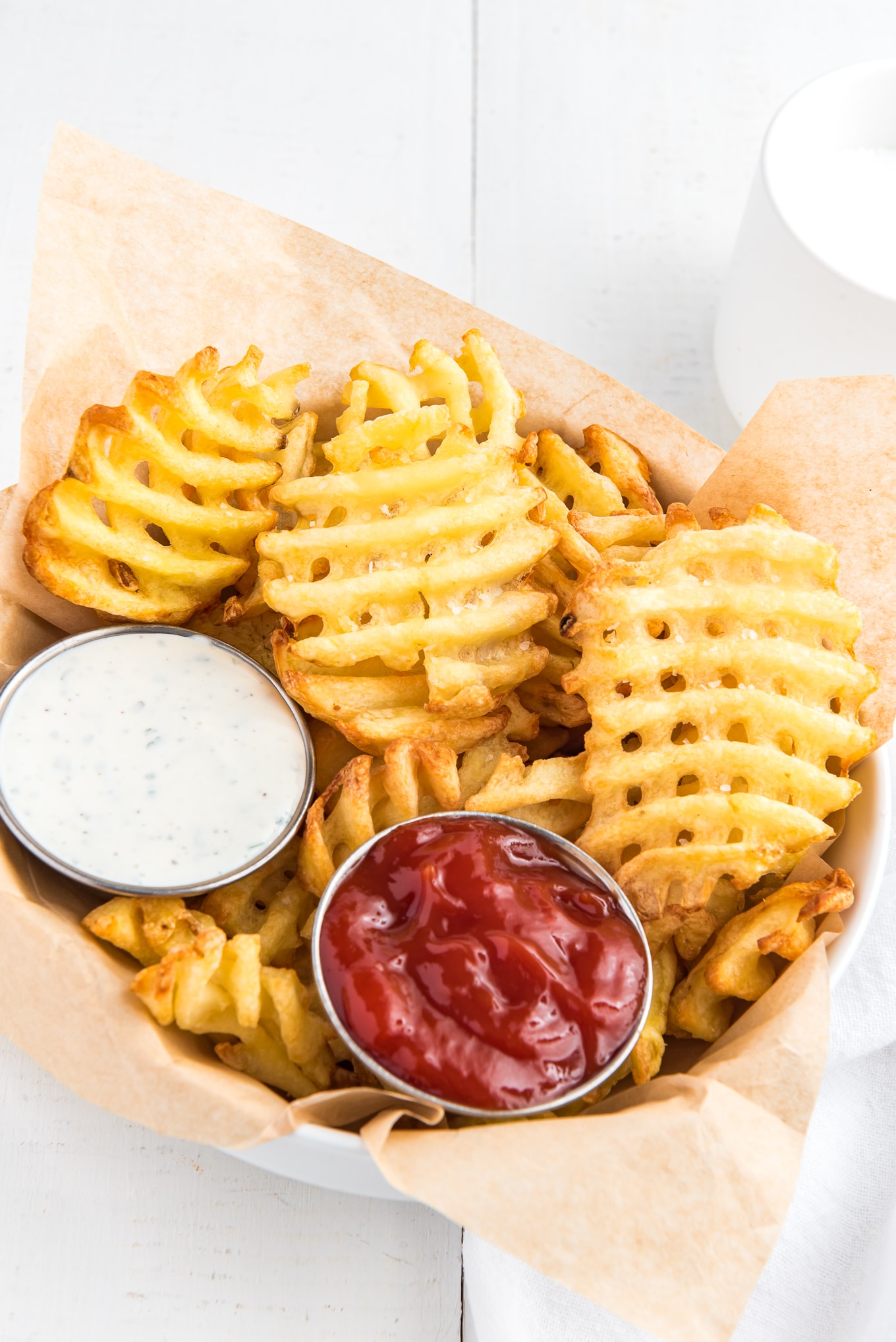 A parchment paper lined basket with waffle fries and condiments. 