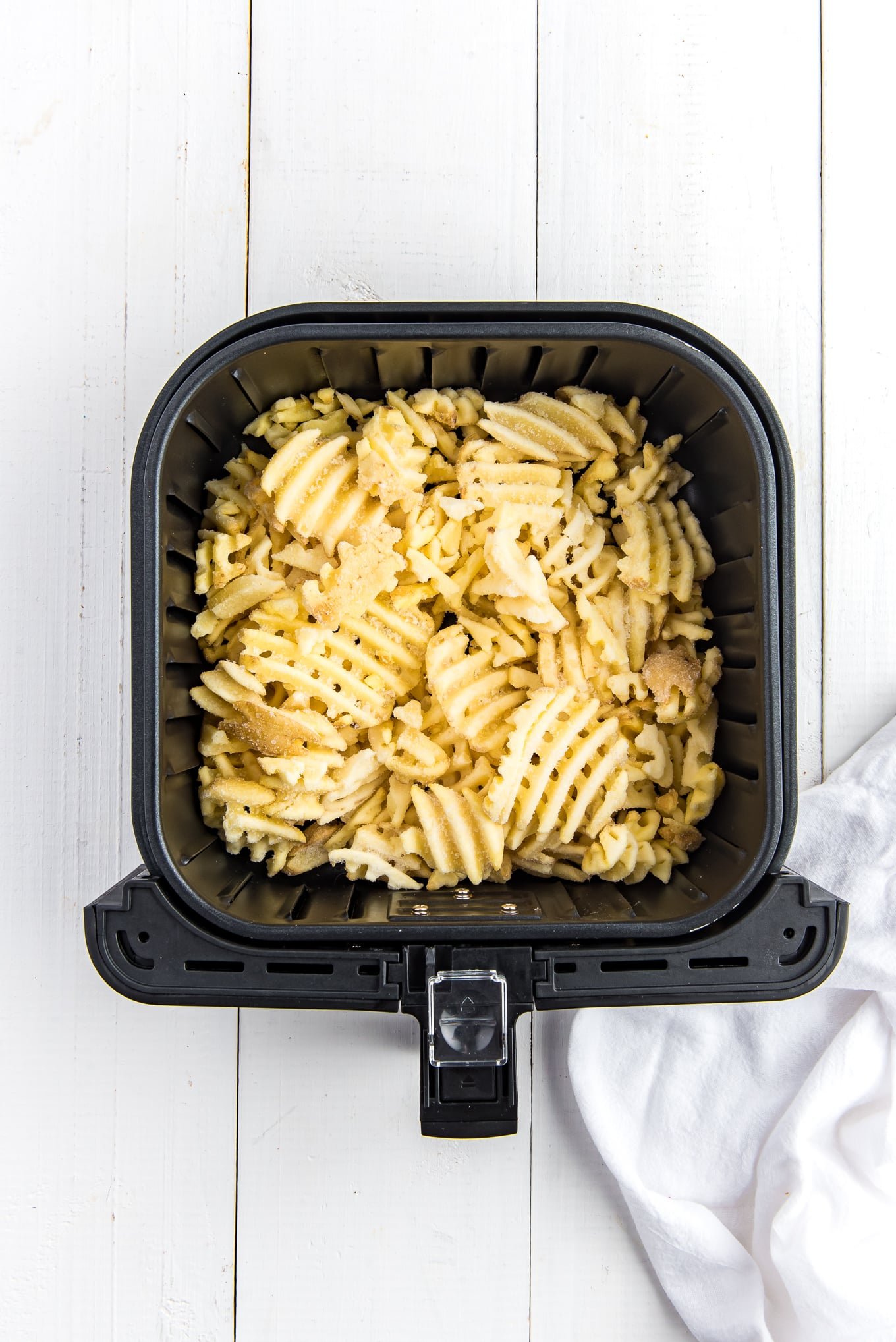 An air fryer basket with waffle fries at the bottom. 