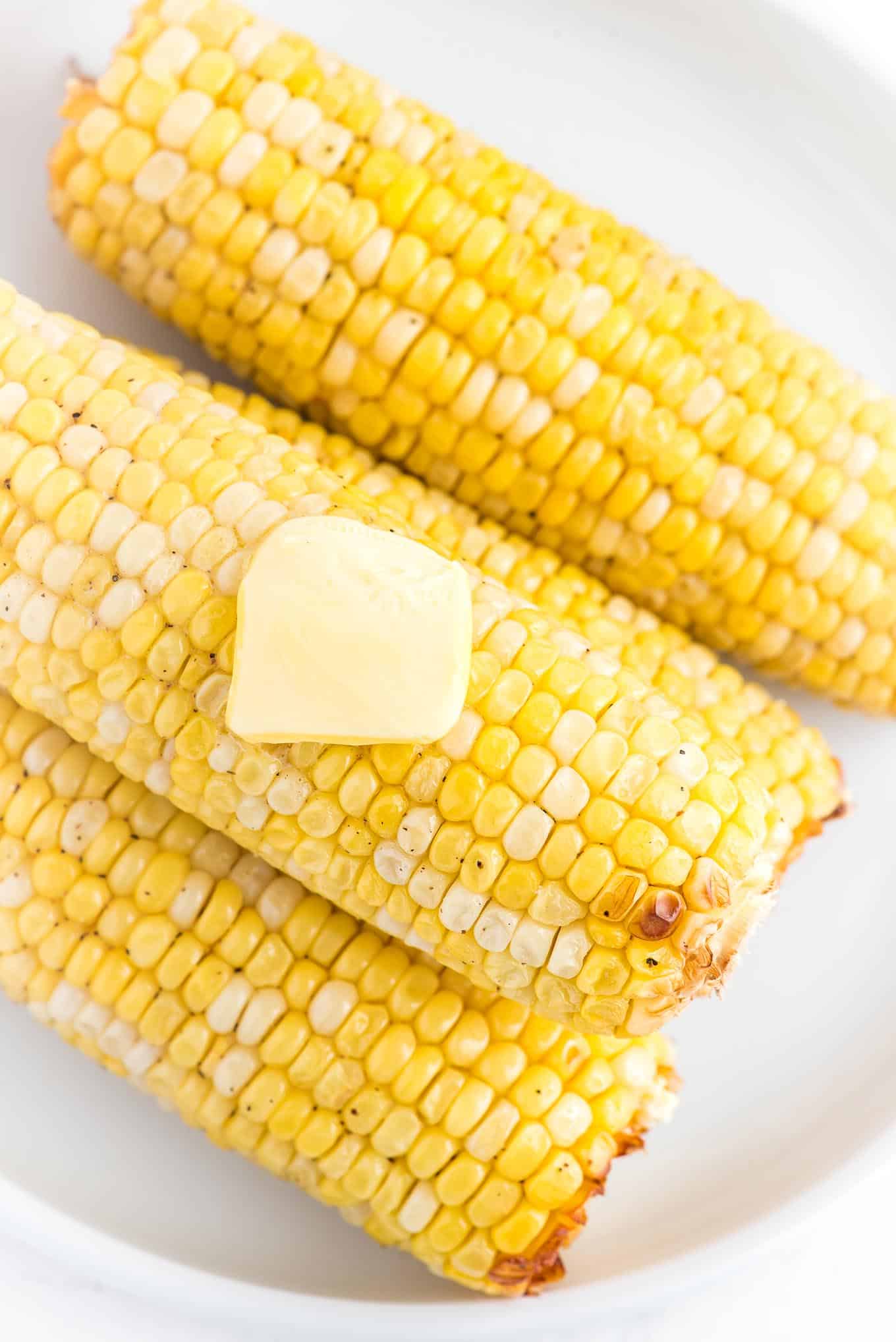 Cooked fresh corn with a pat of butter on the top on a serving platter.