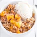 Bisquick peach cobbler in a bowl with a scoop of vanilla ice cream.