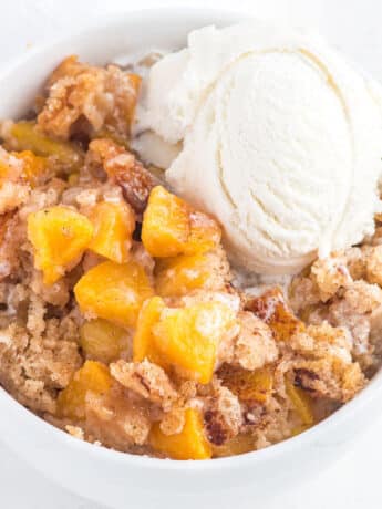 Bisquick peach cobbler in a bowl with a scoop of vanilla ice cream.