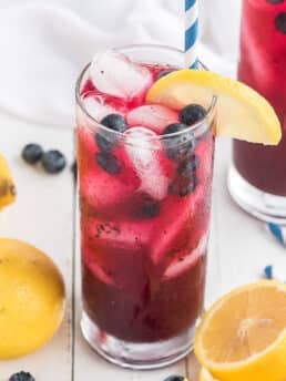 An up-close shot of blueberry lemonade of the counter surrounded by lemons and blueberries.