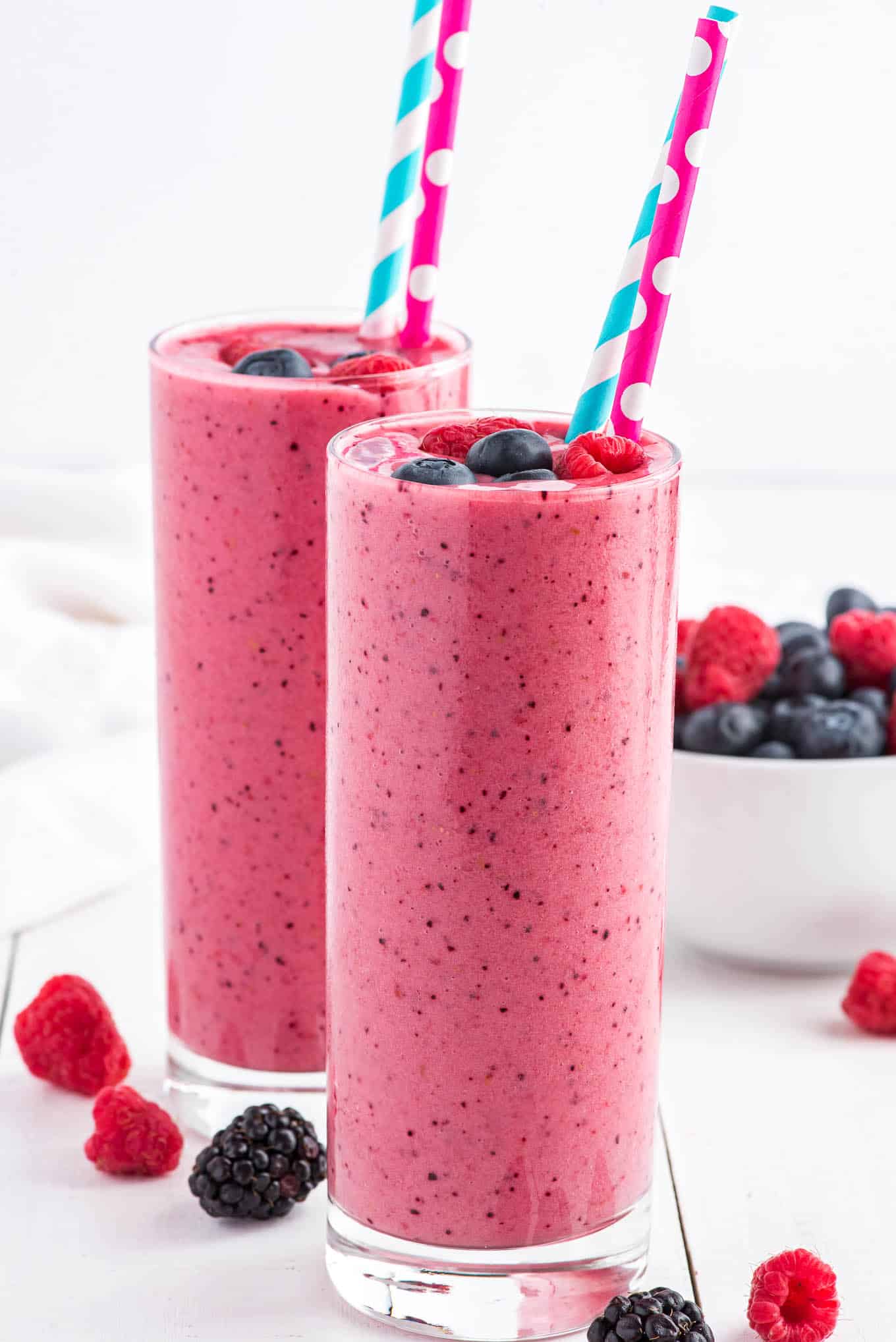 Two glasses of morning smoothies on the table with fresh berries and straws.