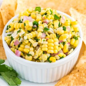 Chipotle corn salsa in a bowl with chips and a leaf of cilantro.