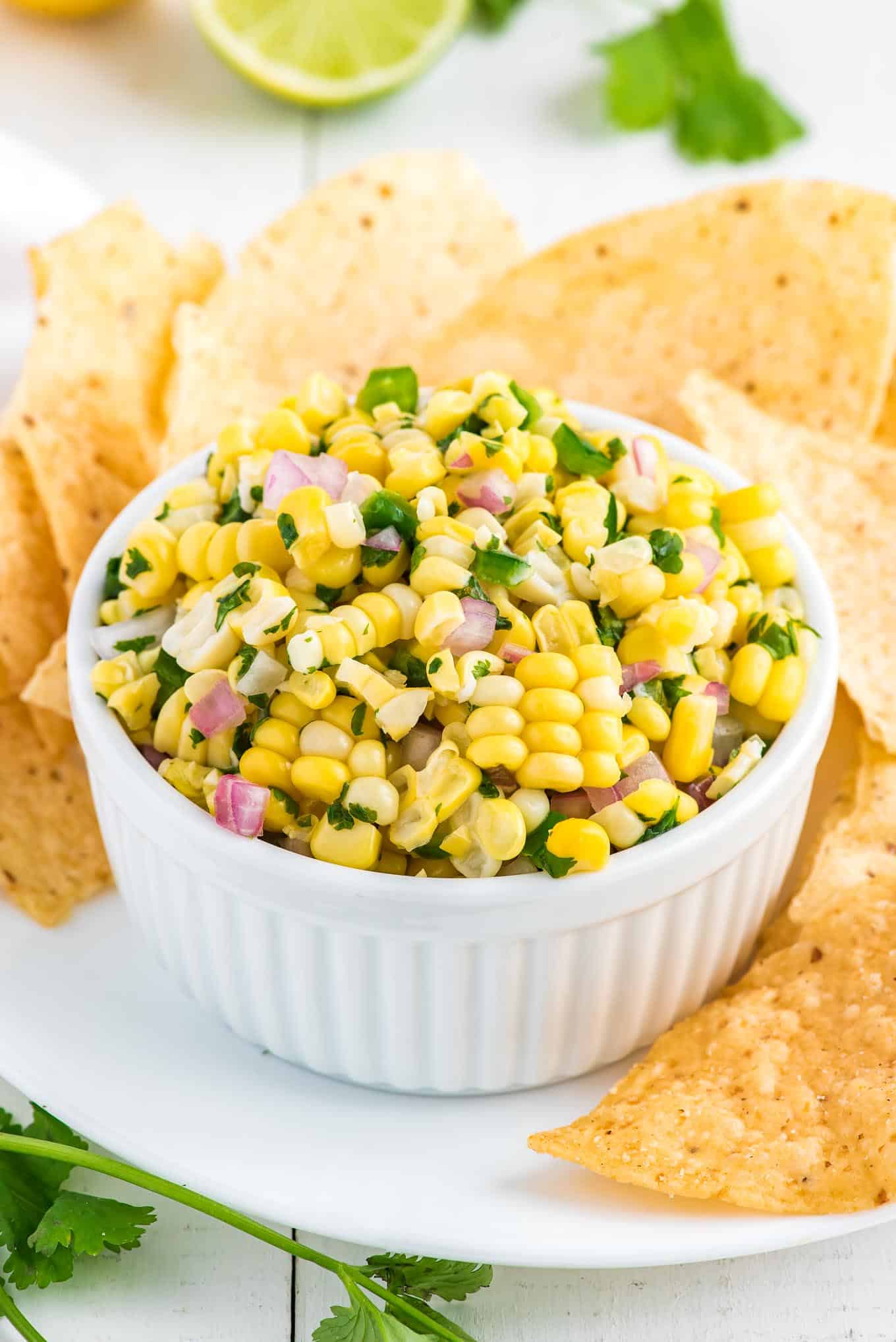 Fresh corn salsa in a bowl on the table with chips around it.
