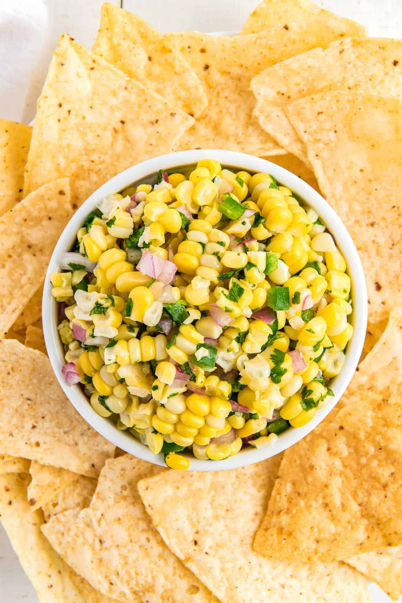 Corn salsa chipotle in a bowl on the table with tortilla chips surrounding the bowl.