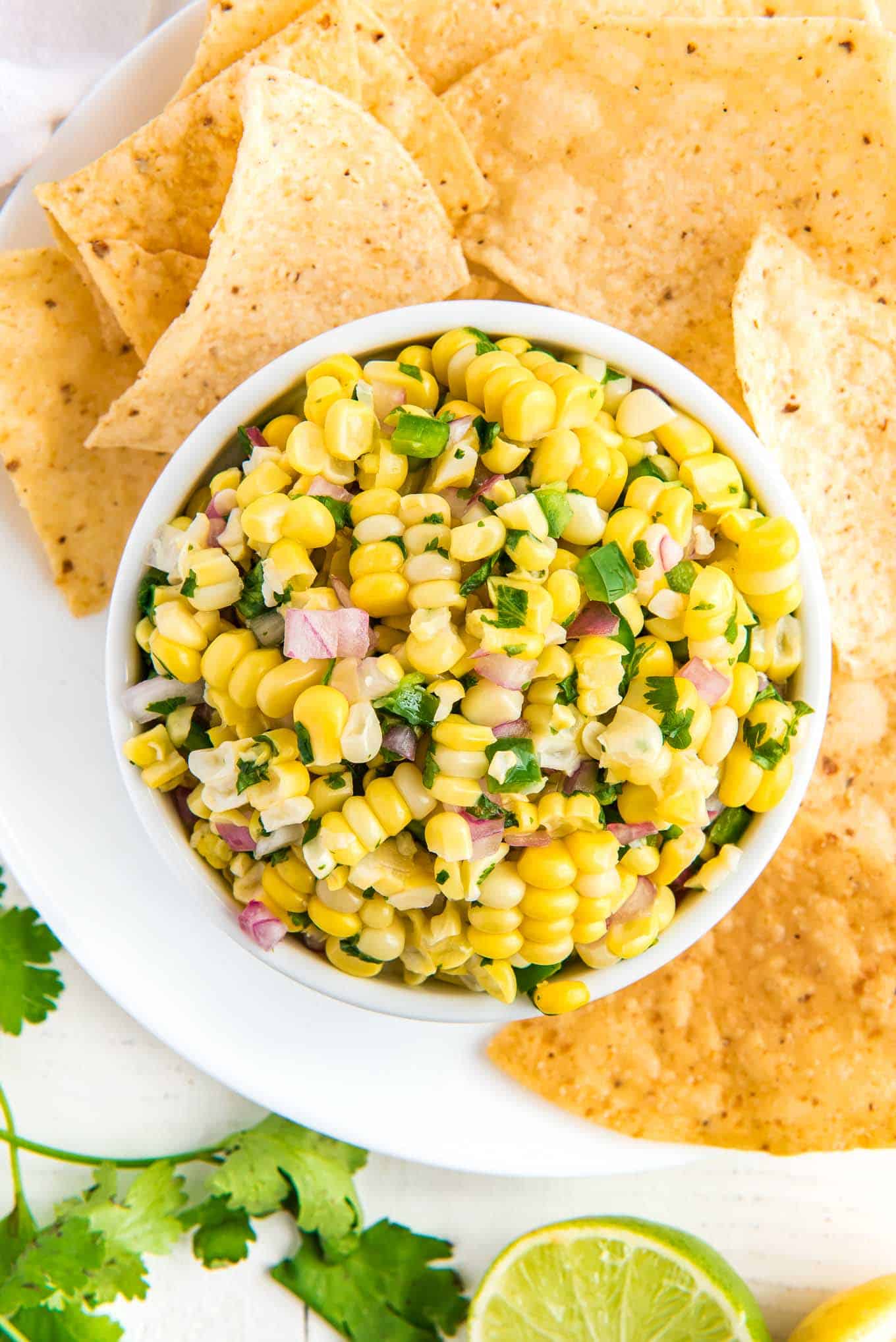 A bowl of copycat corn salsa on a plate surrounded by tortilla chips.