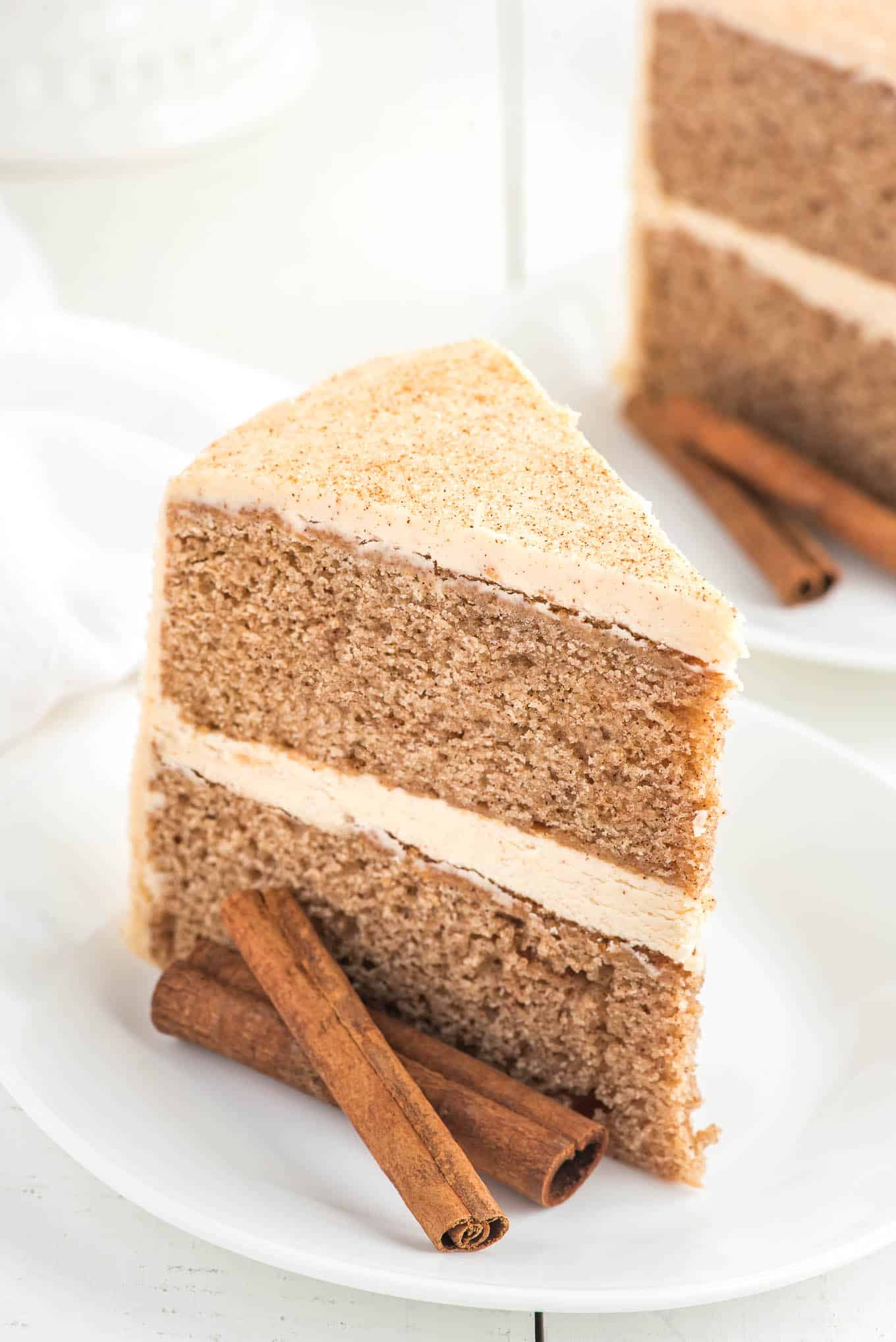 A two-layer cinnamon cake topped with cinnamon buttercream frosting sliced on a plate. 