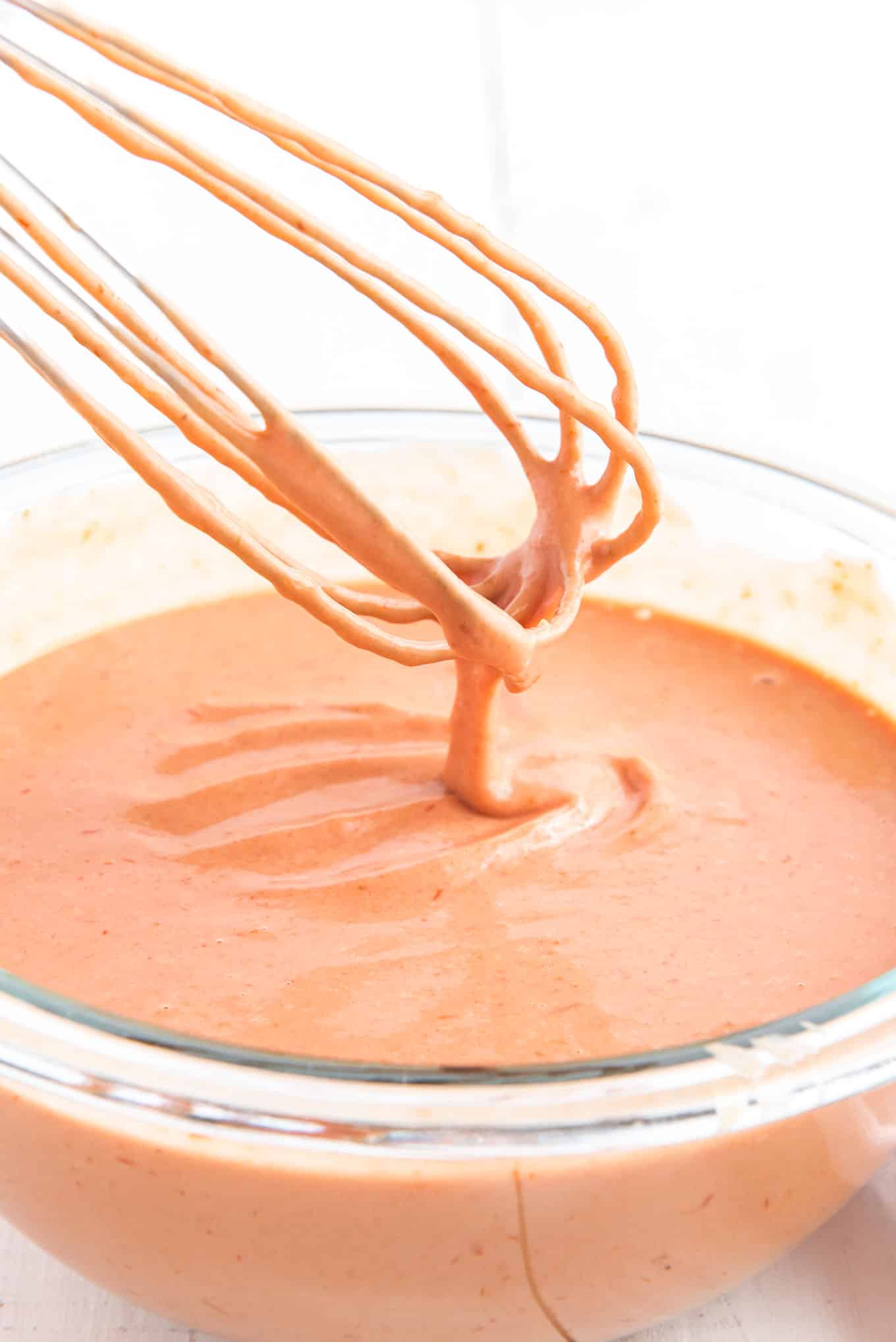 A whisk held up over the bowl of french fry dipping sauce.