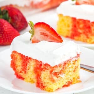 A piece of strawberry jello poke cake with whipped cream frosting on a plate.