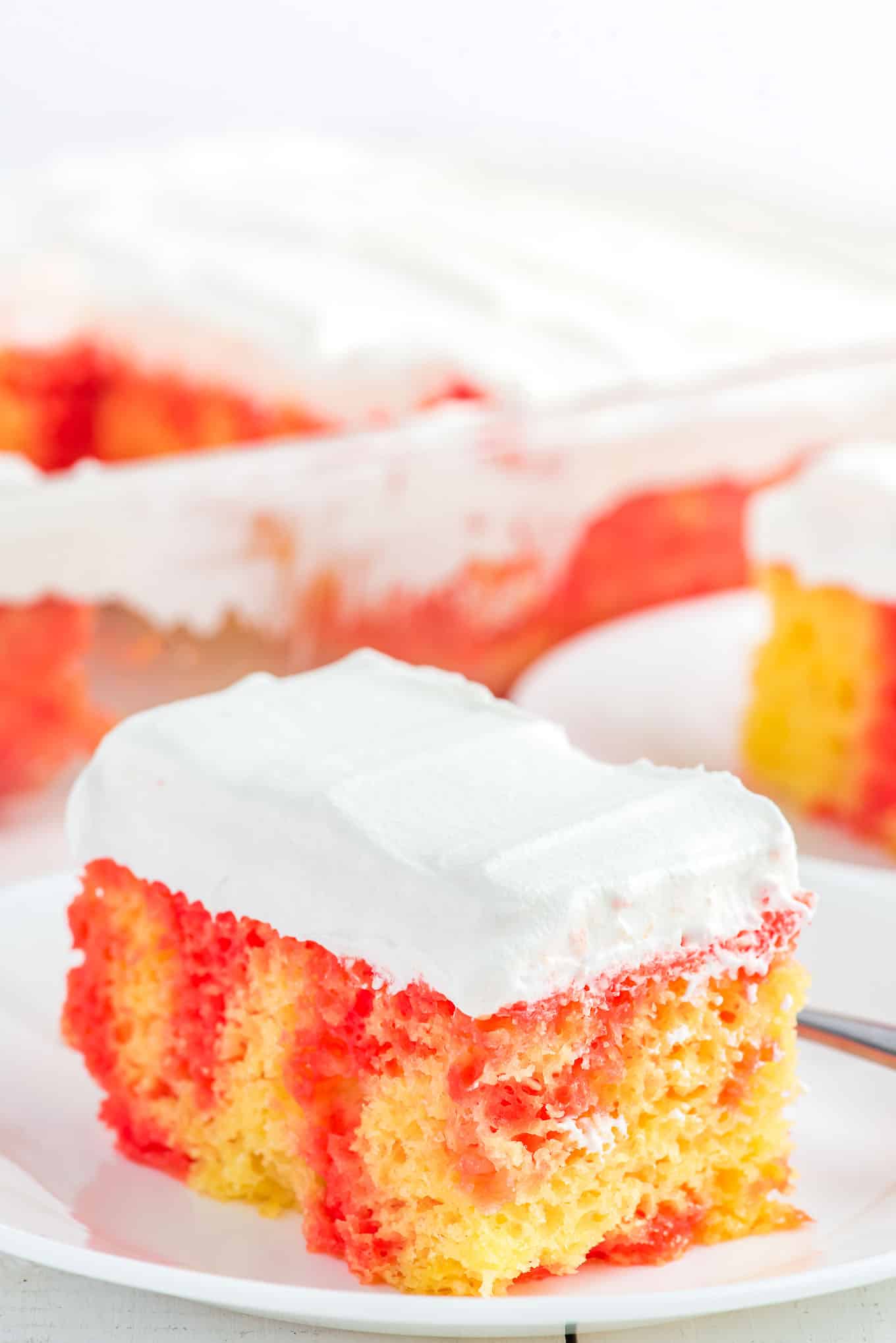 A square of strawberry and lemon cake on a plate topped with whipped cream frosting.