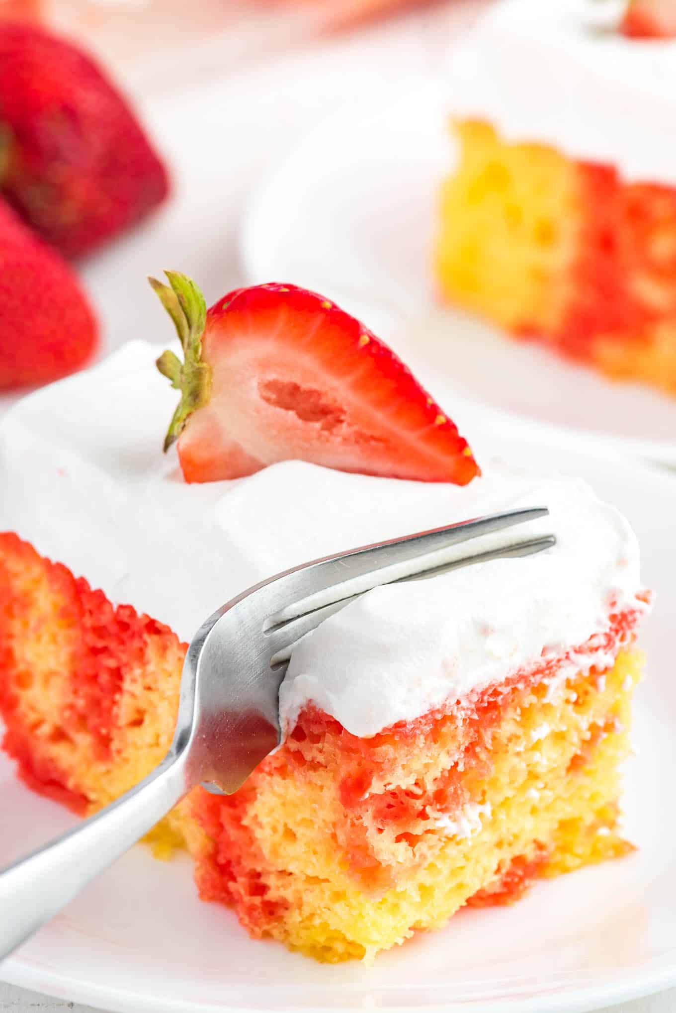 A fork cutting into a corner of a piece of strawberry lemonade poke cake.