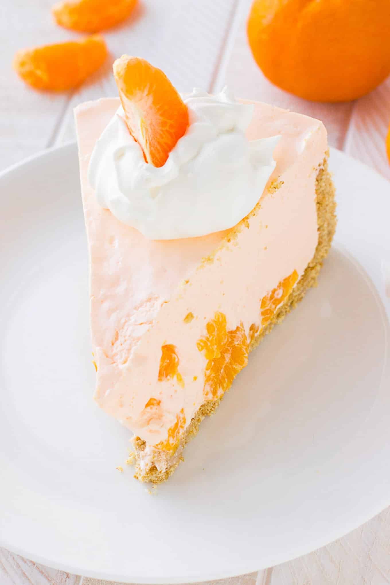 A slice of no-bake orange pie on a plate with some whipped cream and an orange slice.