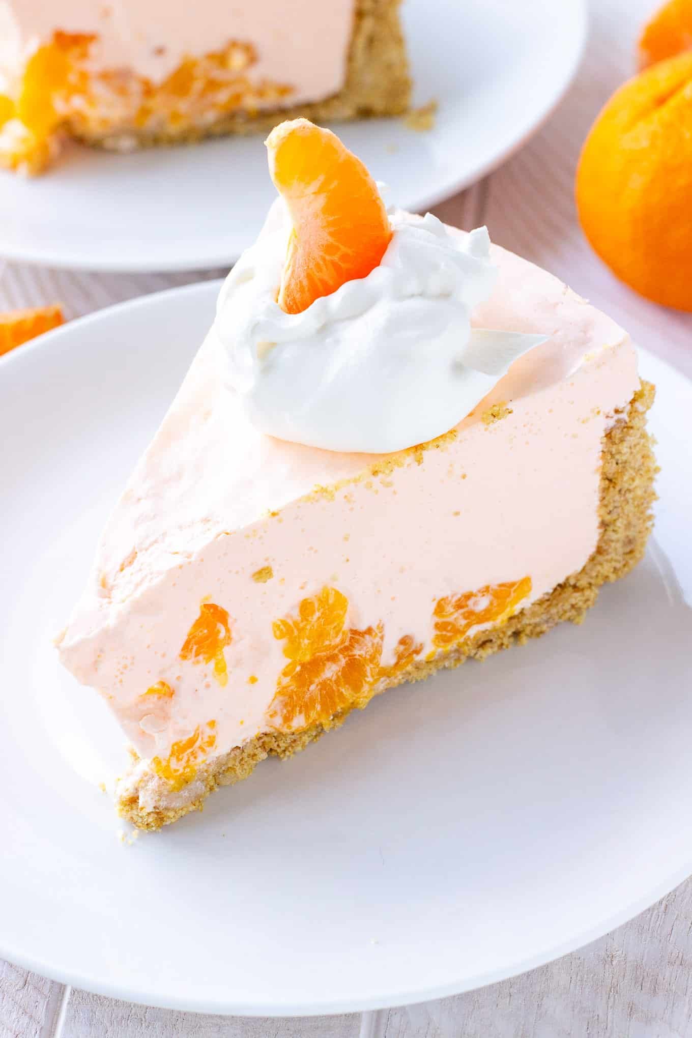 A slice of orange creamsicle pie on a plate topped with whipped cream and a mandarin orange.