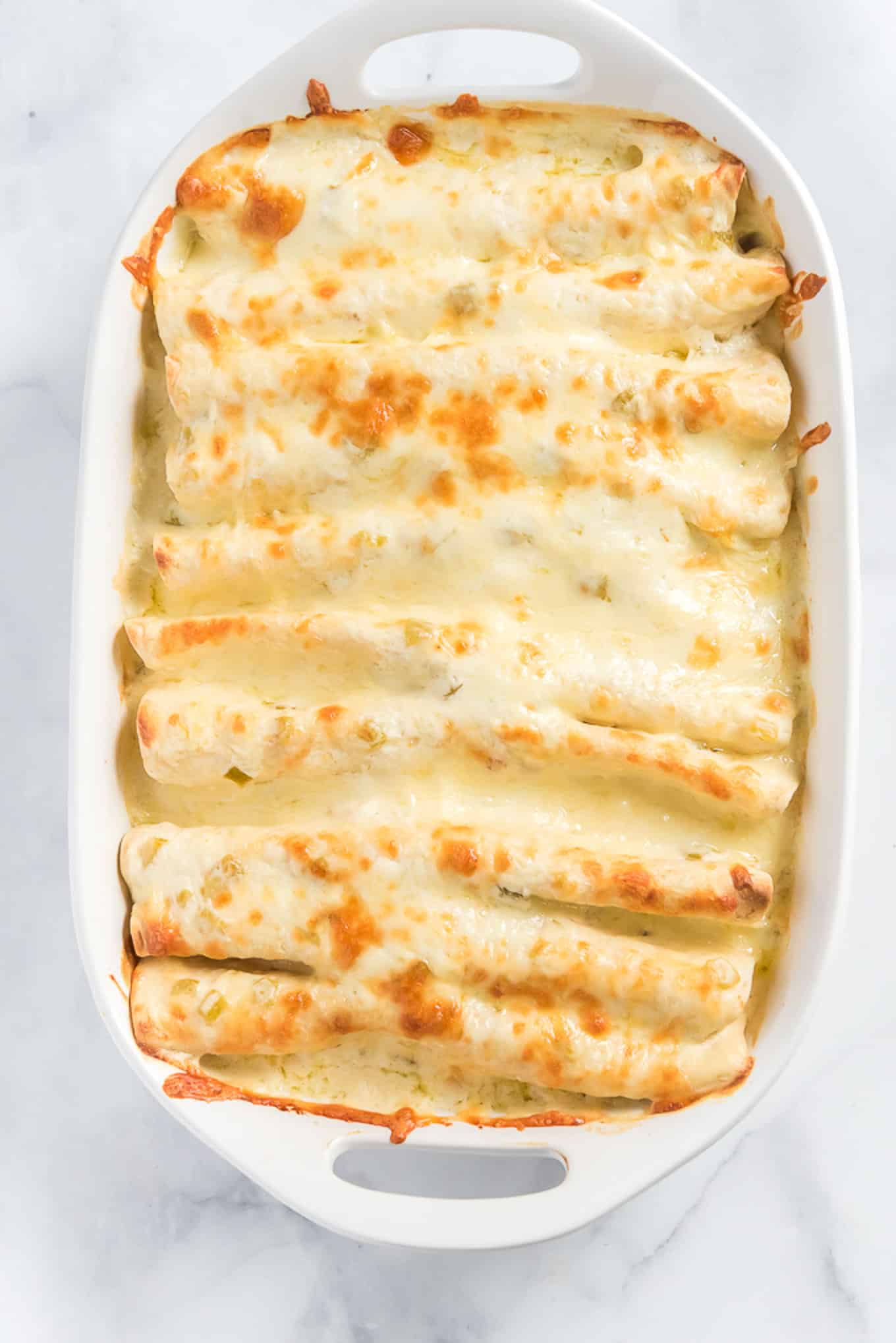 Baked chicken enchiladas in a baking dish on the table.