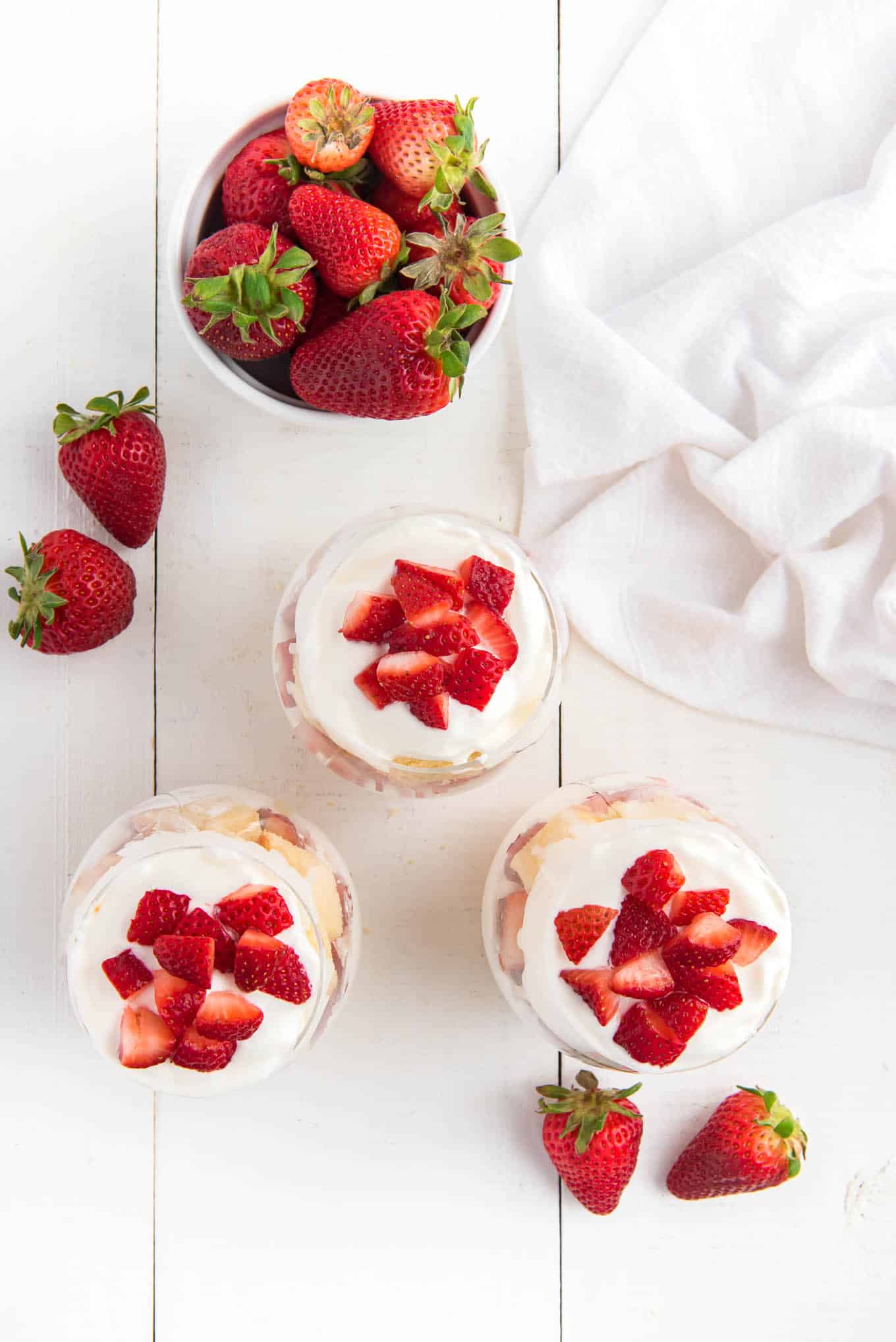 An overhead shot of clear glasses of strawberry shortcake cups with strawberries on a counter.