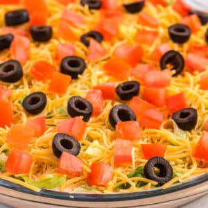 Cold taco dip in a pie plate topped with shredded cheese, olives and tomatoes.