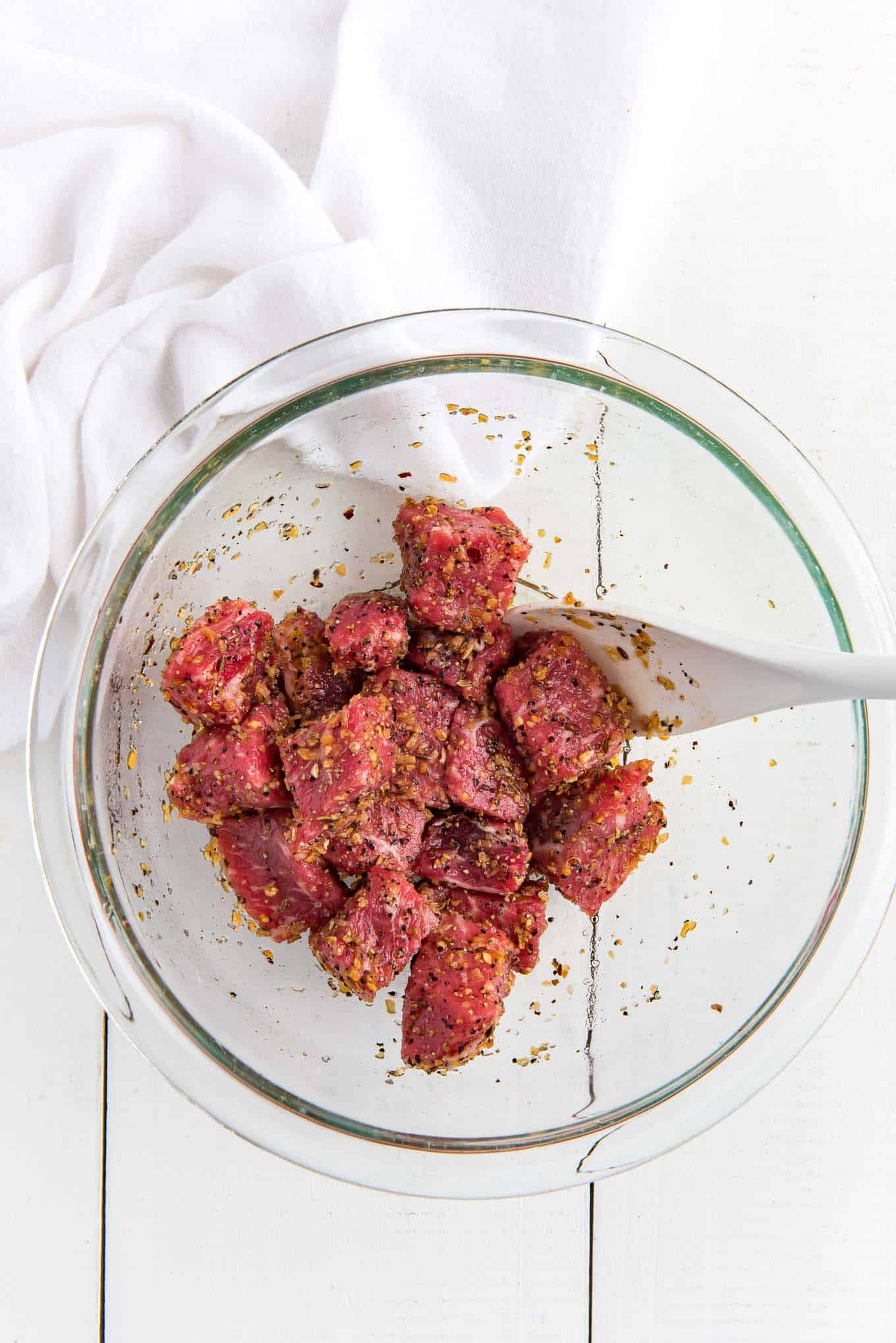 Steak bites with oil and seasoning in a bowl with a spoon.