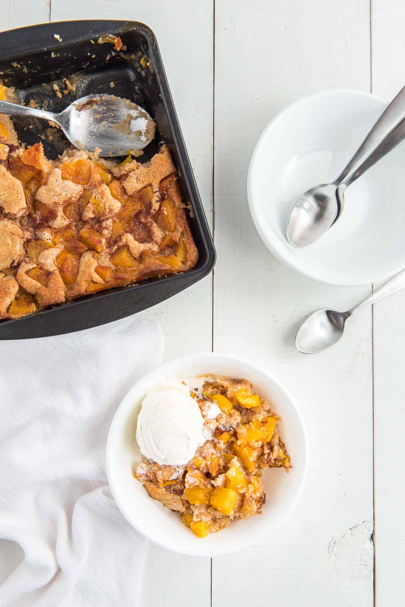 pan of peach cobbler with a bowl of peach cobbler with a scoop of vanilla ice cream on top. 
