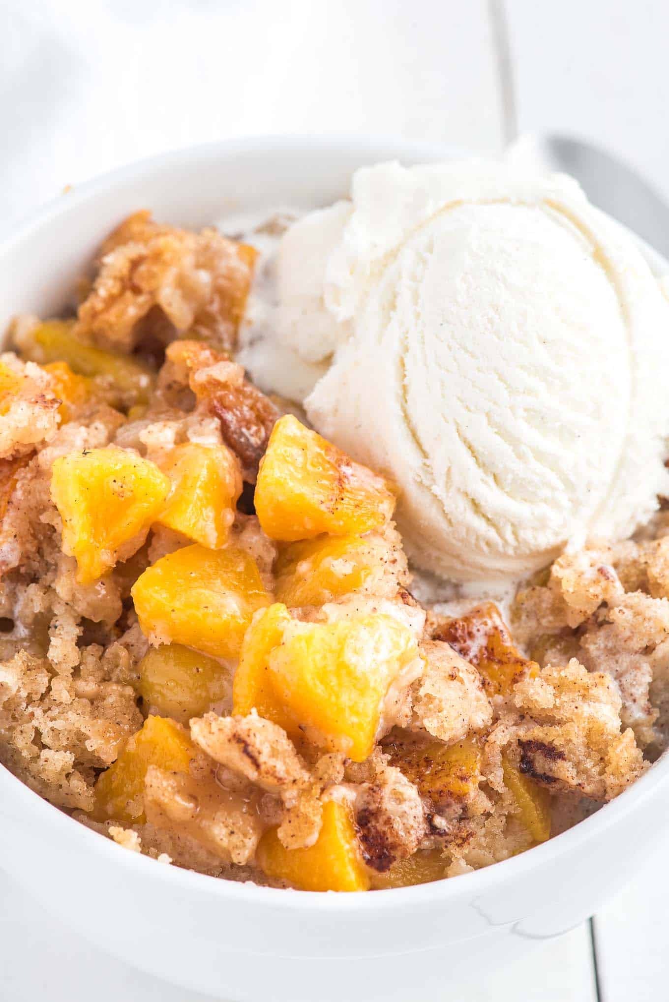 peach cobbler in a bowl with a scoop of vanilla ice cream on top. 